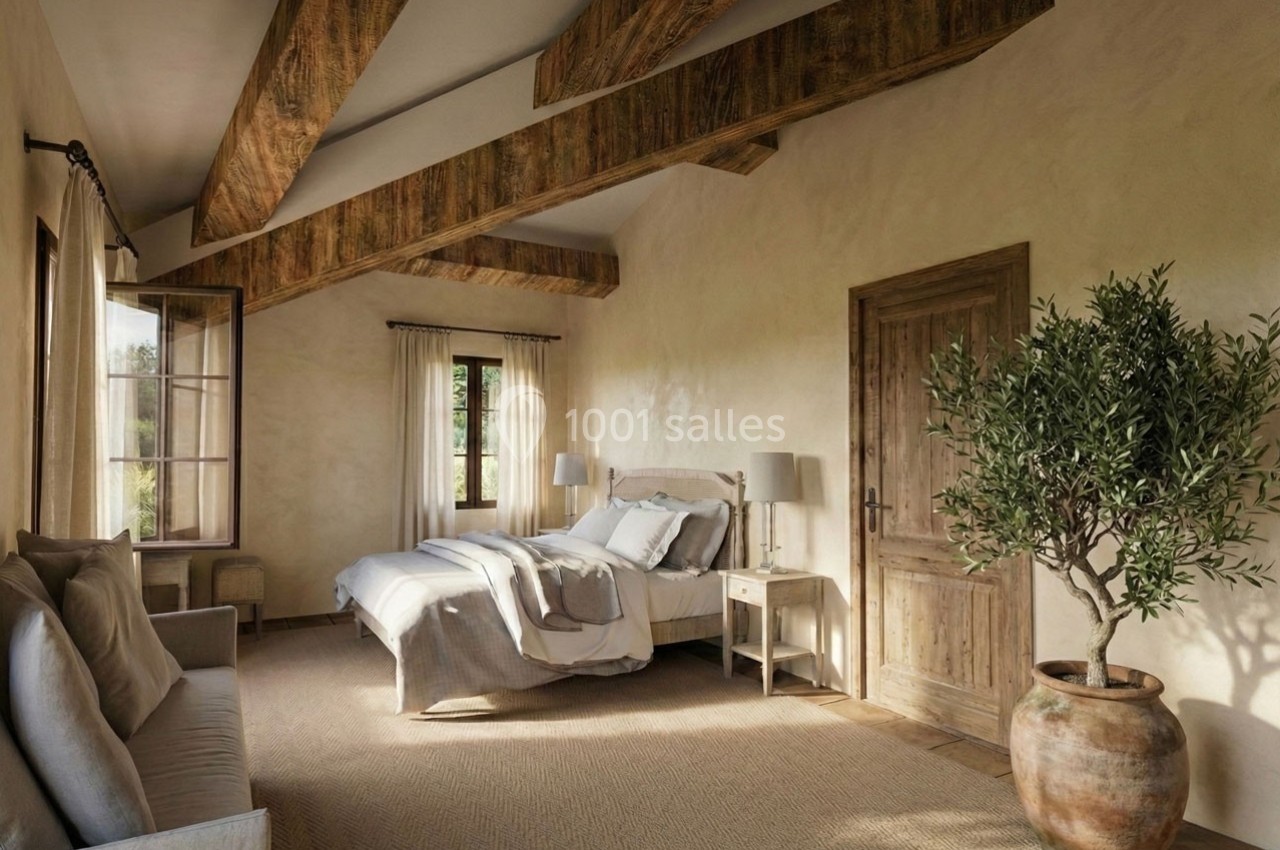 Chambre lumineuse avec poutres en bois, lit double, canapé, grande fenêtre et plante en pot dans un décor chaleureux.