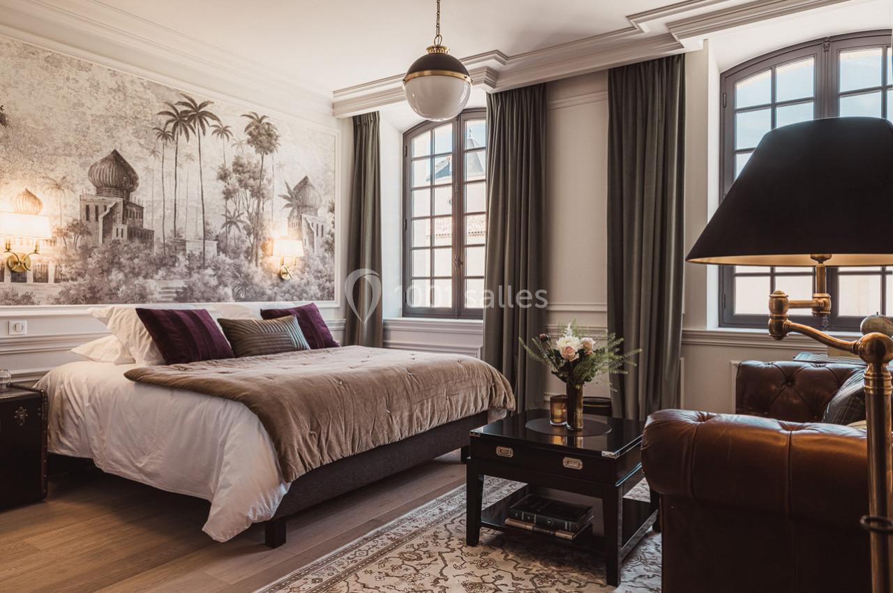Chambre élégante avec lit double, décoration murale exotique, grandes fenêtres et mobilier classique.