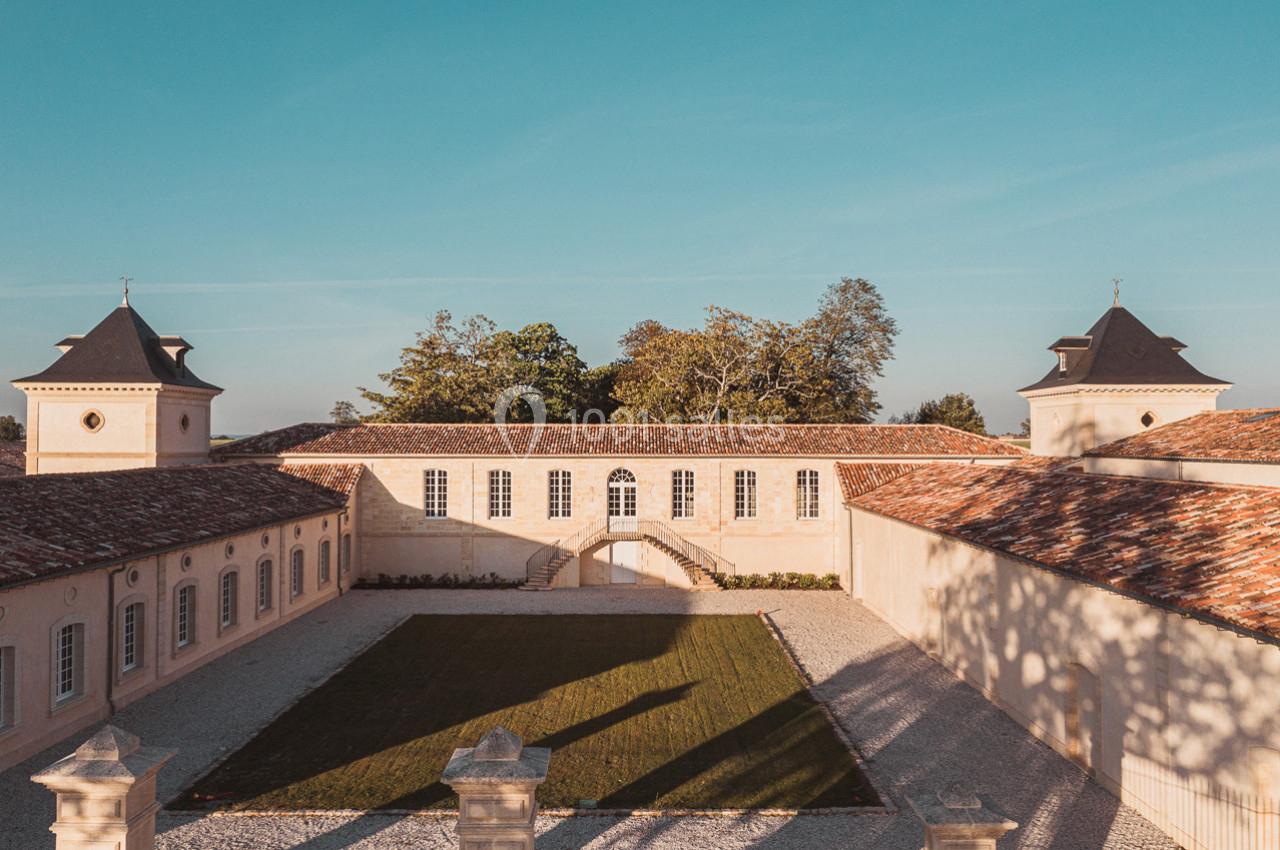 Cour intérieure d'un bâtiment en pierre avec toits en tuiles, encadrée par deux pavillons sous un ciel dégagé.