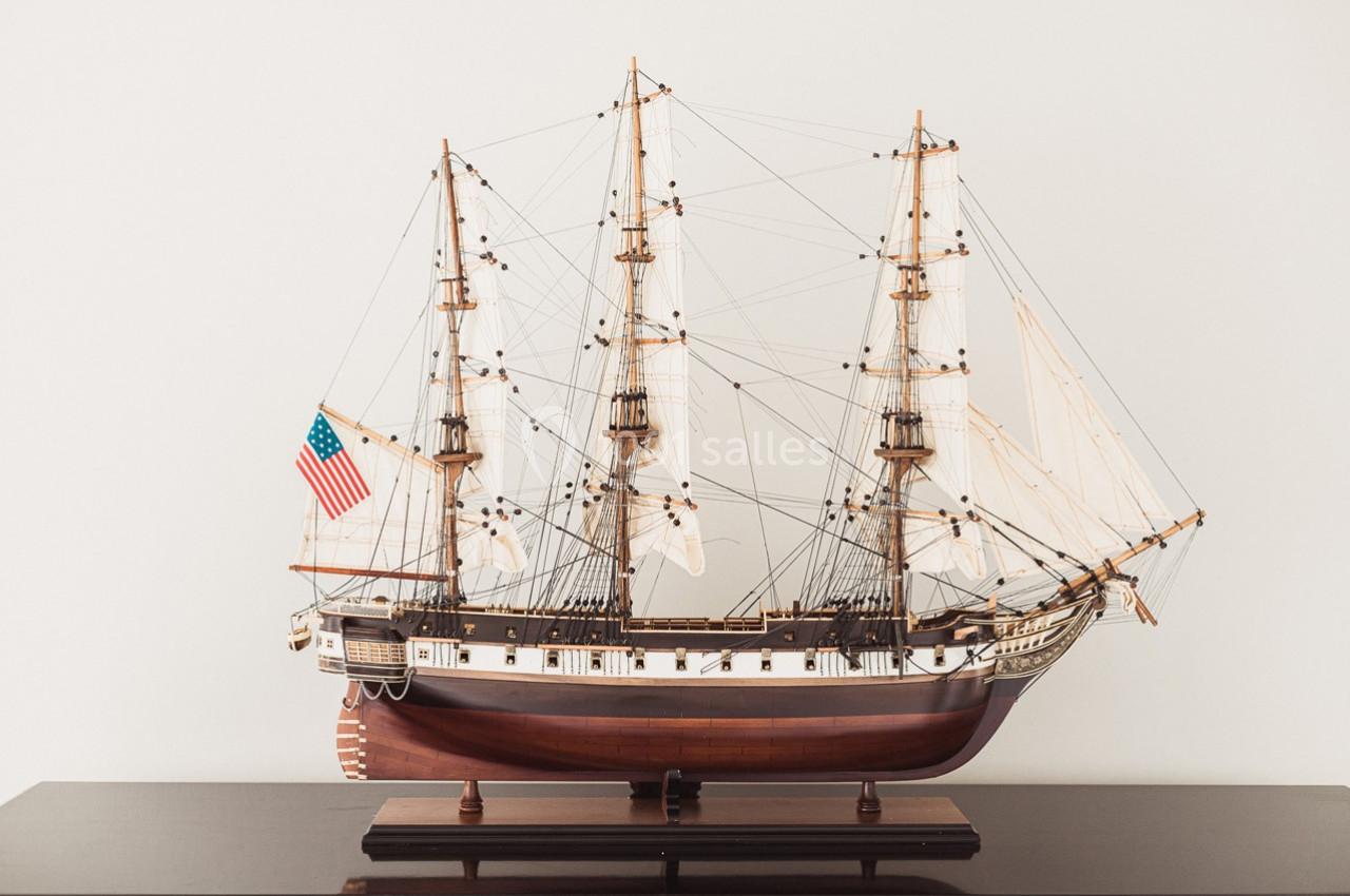 Maquette détaillée d'un voilier ancien avec trois mâts, posée sur une surface sombre, drapeau américain visible.