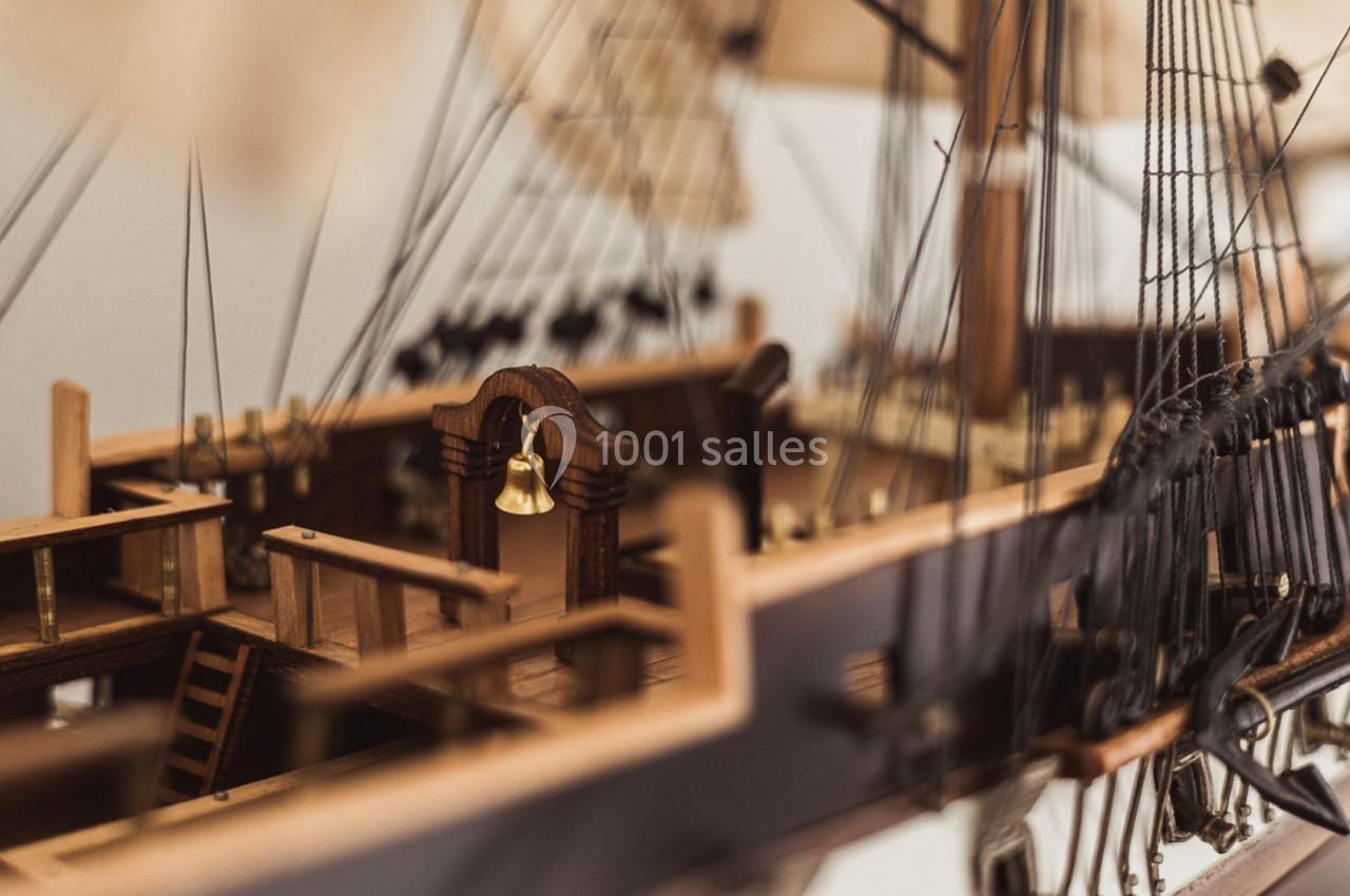 Maquette détaillée d'un navire en bois avec des cordages, une cloche dorée et des éléments de pont visibles.