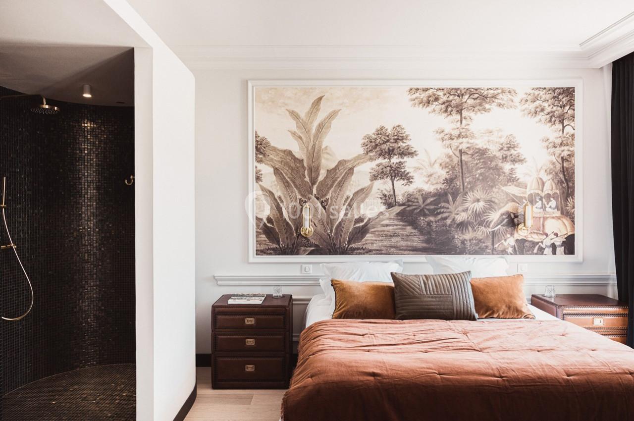 Chambre élégante avec lit double, couvre-lit brun, mur décoré d'une fresque tropicale et douche ouverte à gauche.