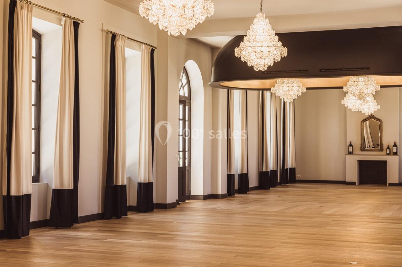 Salle lumineuse avec parquet en bois clair, rideaux bicolores, lustres élégants et cheminée décorative.