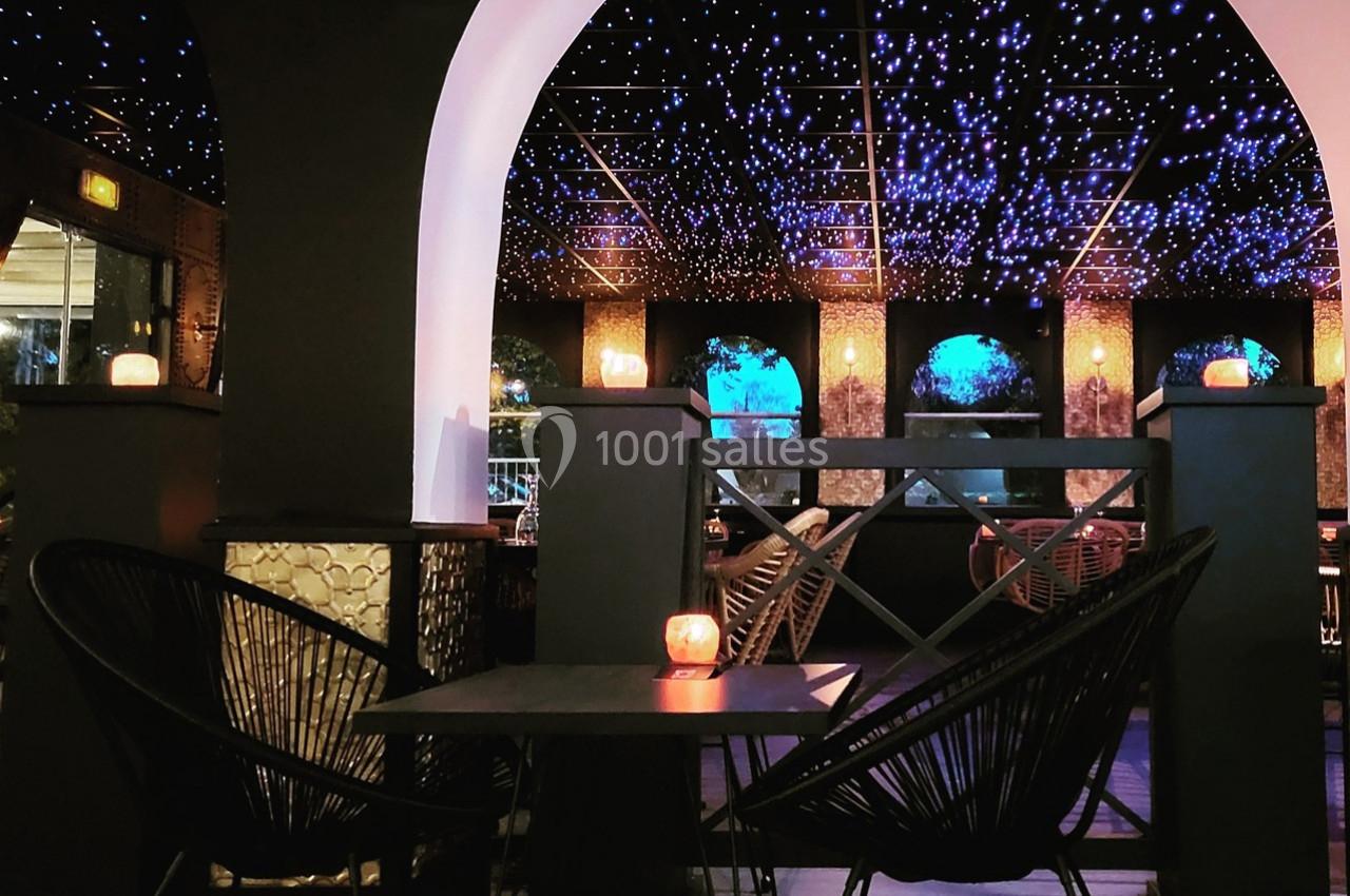 Espace intérieur avec des arches, des fauteuils en rotin et un plafond illuminé de lumières étoilées.
