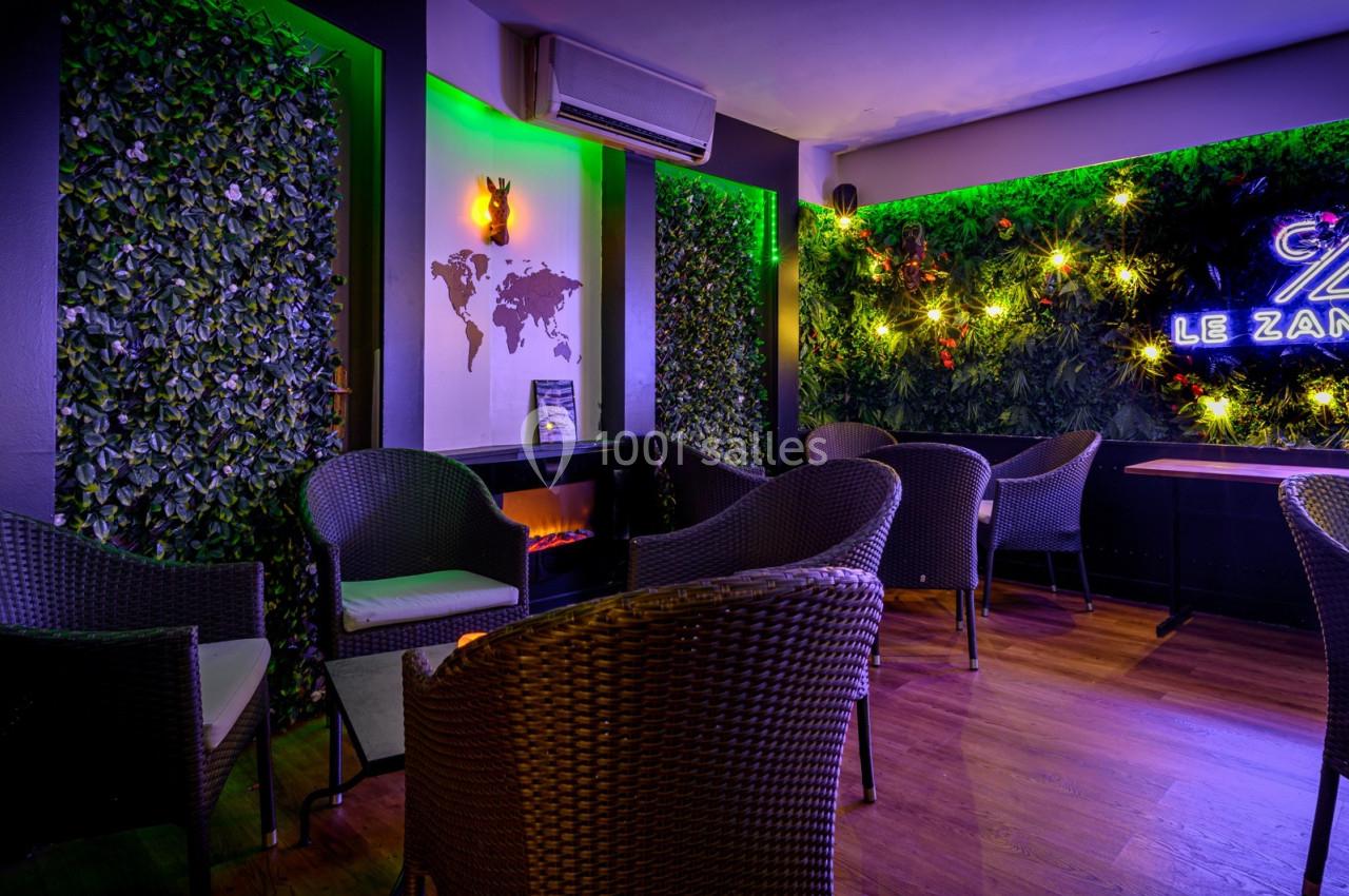 Espace lounge avec fauteuils en rotin, murs végétalisés, éclairage néon et carte du monde en décoration murale.