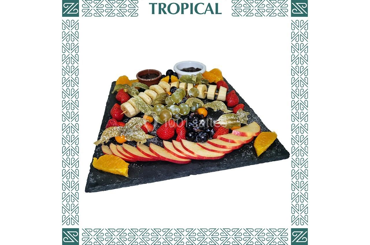 Plateau de fruits variés avec pommes, raisins, baies, tranches d'orange et sauces, présenté sur une ardoise noire.