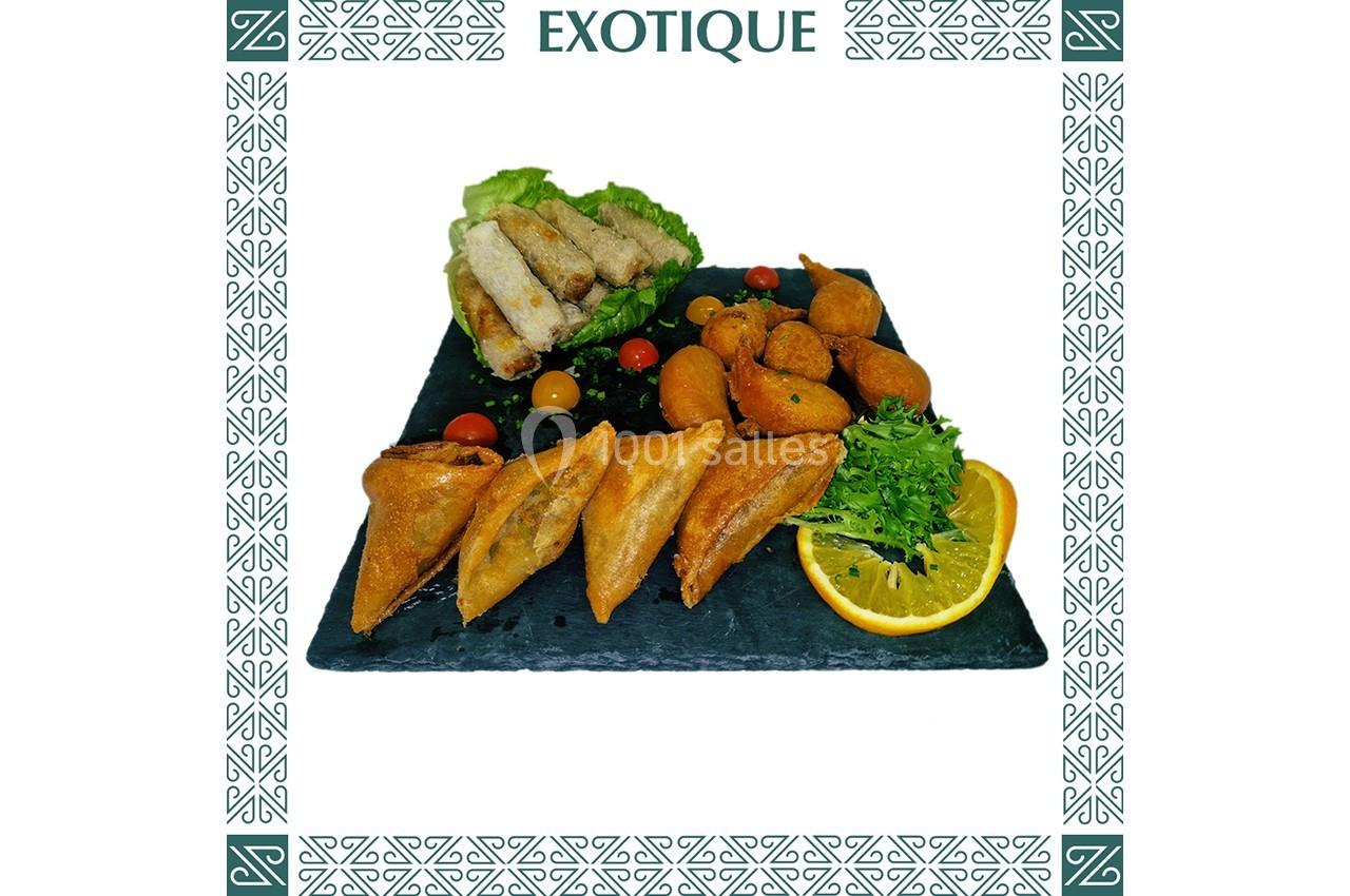 Assortiment de samoussas, nems, accras et crudités disposés sur une ardoise avec une tranche d'orange.