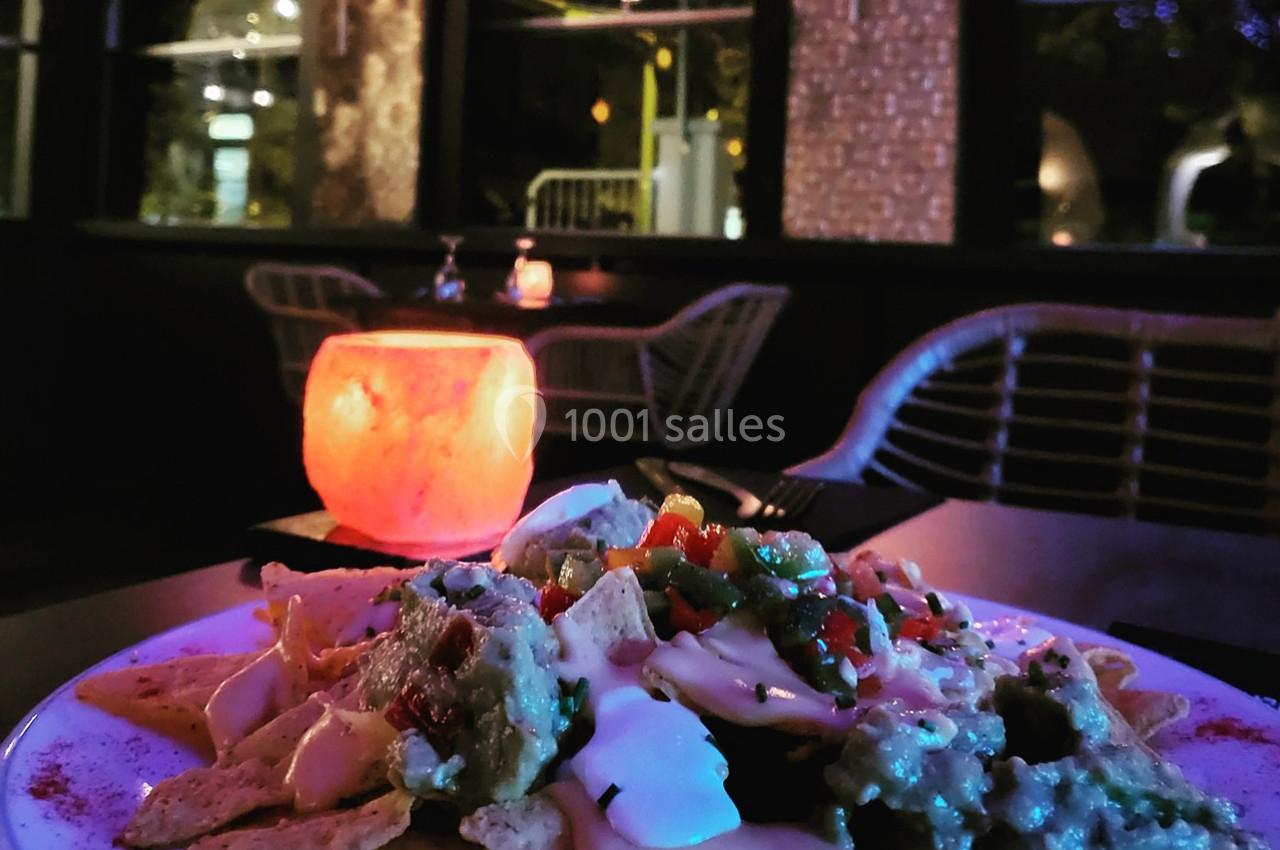 Assiette de nachos garnis de sauces et légumes, posée sur une table dans un restaurant à l'éclairage tamisé.