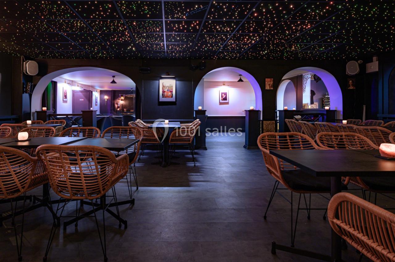 Salle de restaurant avec des tables en bois, chaises en rotin et plafond éclairé par des lumières étoilées.