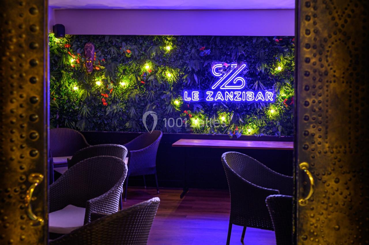 Mur végétal éclairé avec un néon ’Le Zanzibar’, entouré de fauteuils en rotin dans une ambiance tamisée.