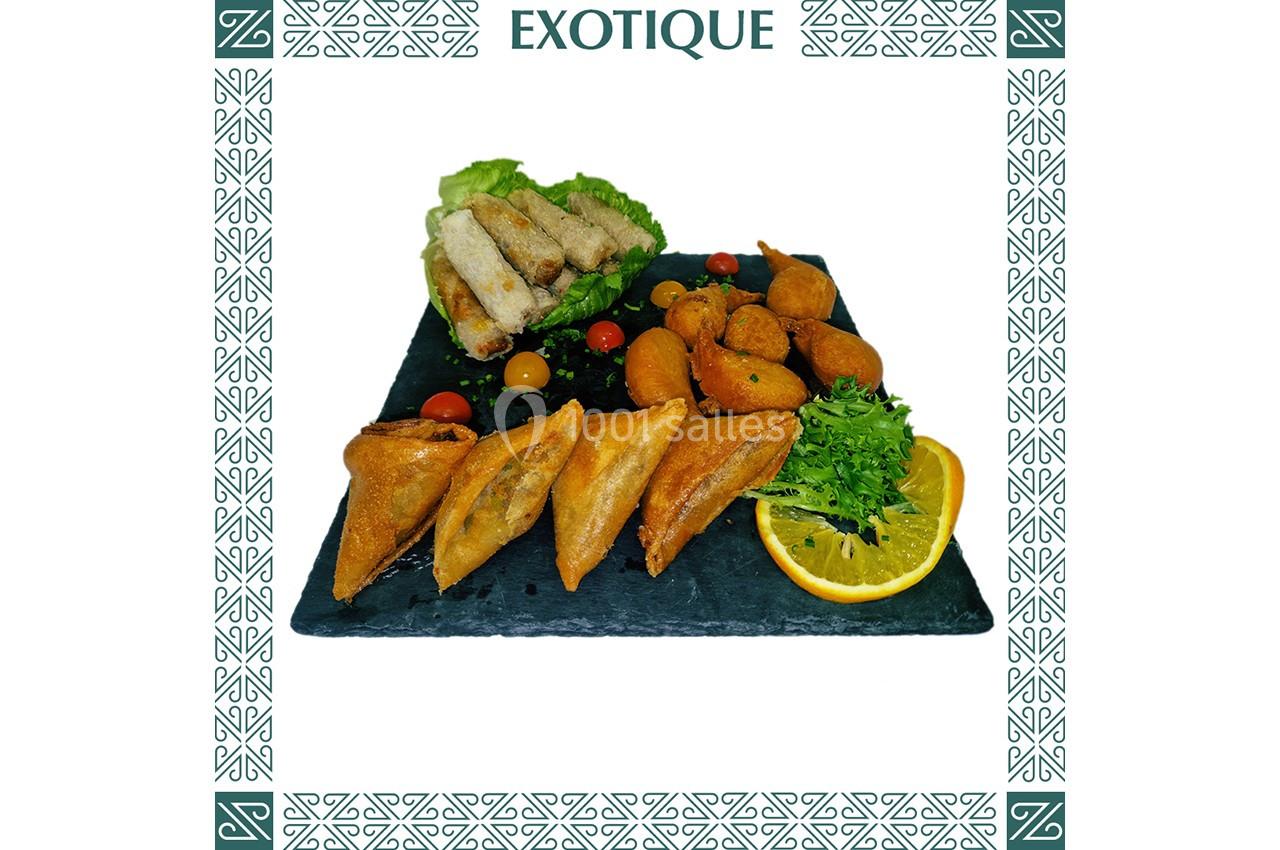 Assortiment de bouchées salées comprenant samoussas, accras, nems, crudités et tranche d'orange sur ardoise.