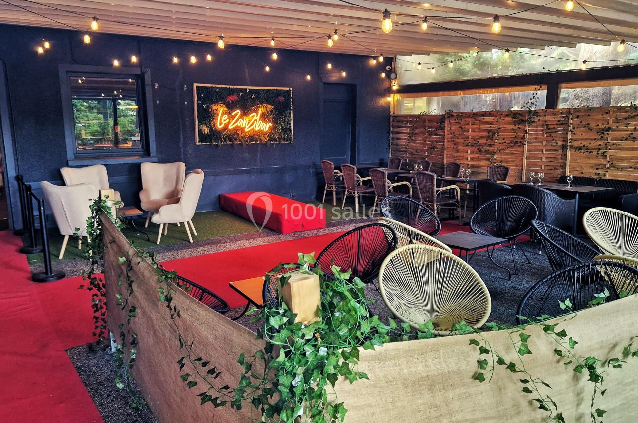 Terrasse couverte avec fauteuils, tables, guirlandes lumineuses et décoration végétale dans une ambiance chaleureuse.