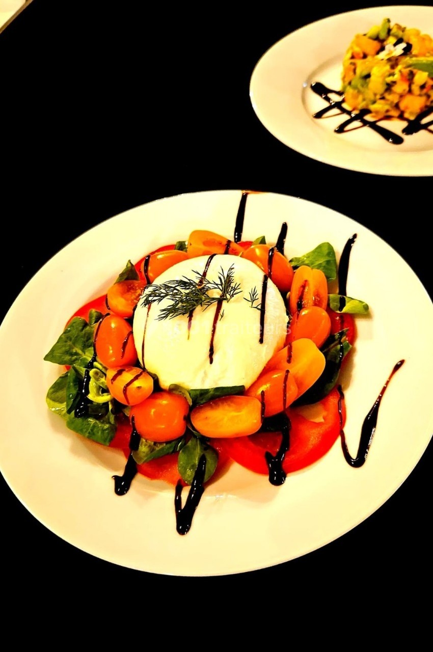 Assiette de burrata avec tomates cerises, roquette et filet de vinaigre balsamique, servie sur une table noire.