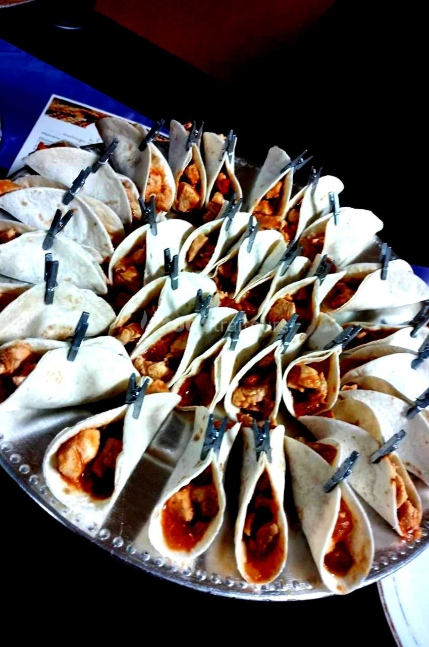 Plateau de mini-tacos garnis de viande et sauce, maintenus ouverts par des pinces, disposés en cercle.