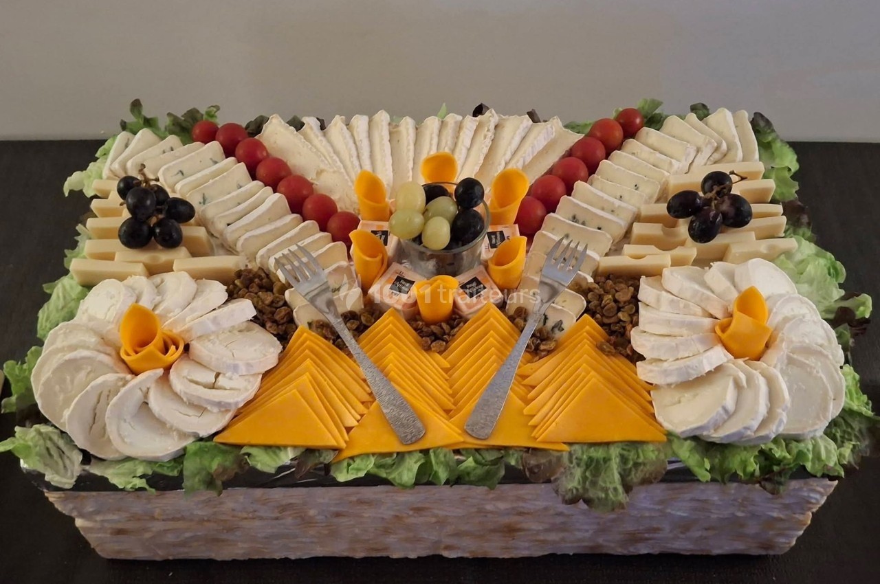 Plateau de fromages variés joliment disposés avec raisins, tomates cerises et décorations sur un lit de salade verte.