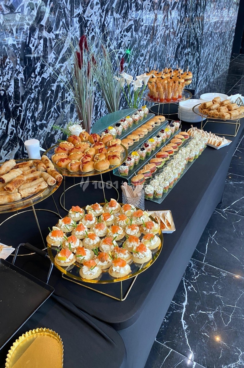 Buffet de pièces cocktail variées avec canapés, roulés, mini-sandwichs et verrines sur une table noire.