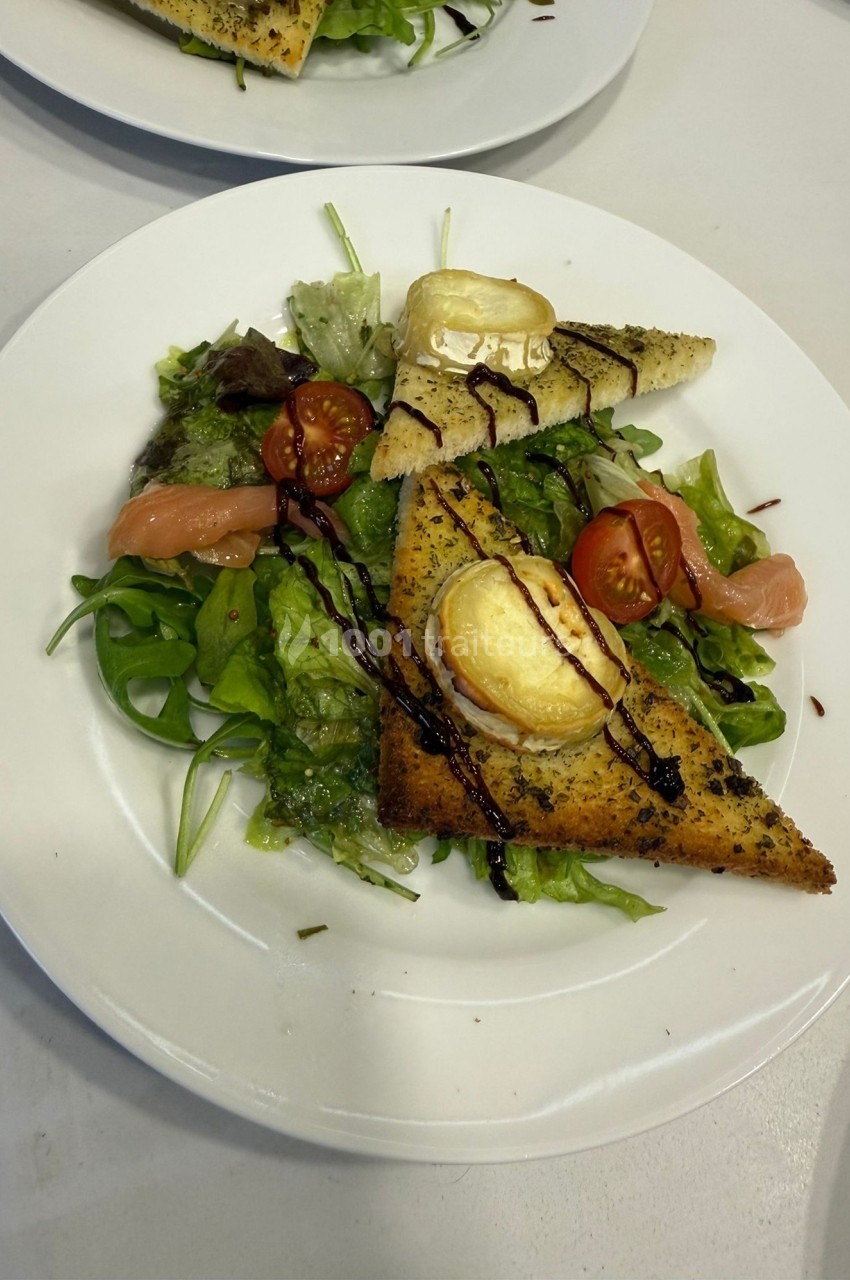 Assiette de salade verte garnie de toasts au fromage, tomates cerises, saumon fumé et filet de sauce balsamique.