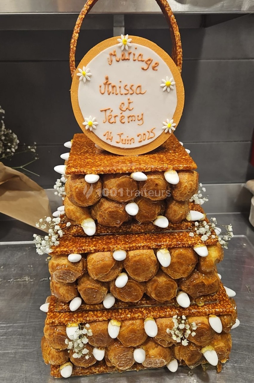 Pièce montée en choux décorée de fleurs et d'amandes, avec une plaque indiquant un mariage le 14 juin 2025.
