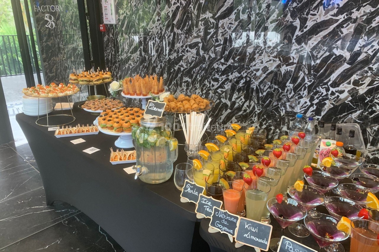 Buffet avec boissons fruitées, verrines, pâtisseries et snacks salés disposés sur une table noire dans un décor moderne.