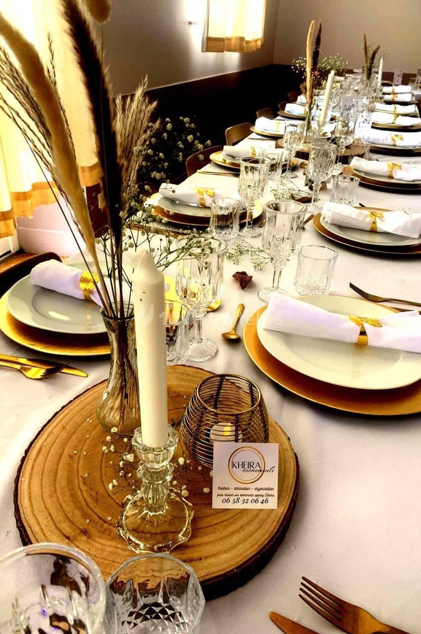 Table élégamment dressée avec des assiettes blanches, des sets dorés, des verres et une décoration florale naturelle.