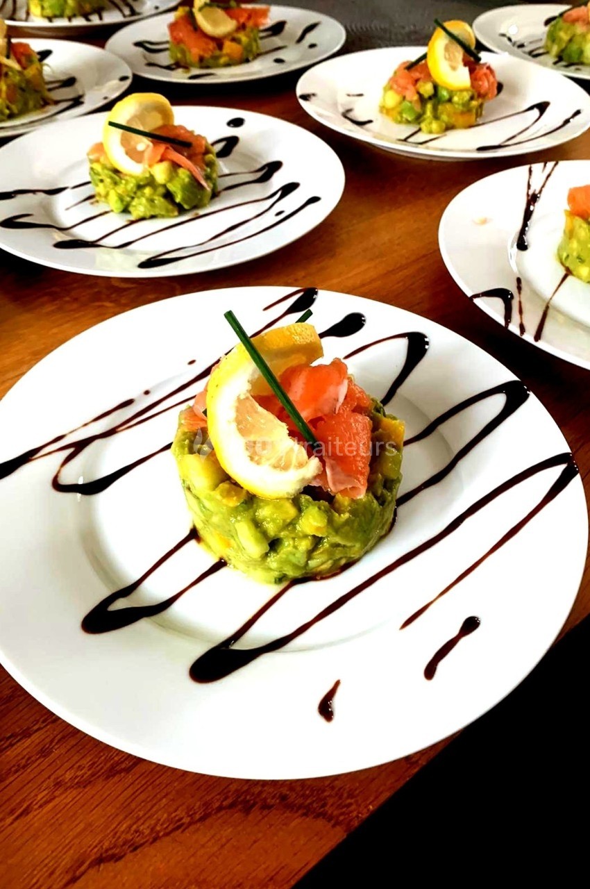 Assiette de tartare d'avocat et saumon fumé, décorée de citron, ciboulette et filet de sauce balsamique.