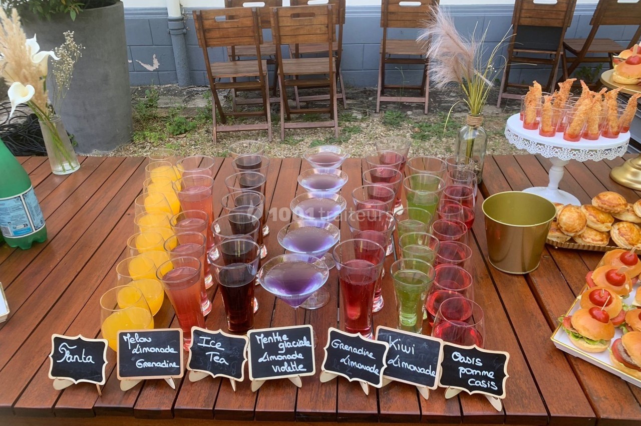 Buffet de boissons colorées disposées sur une table en bois, avec des étiquettes indiquant les saveurs.