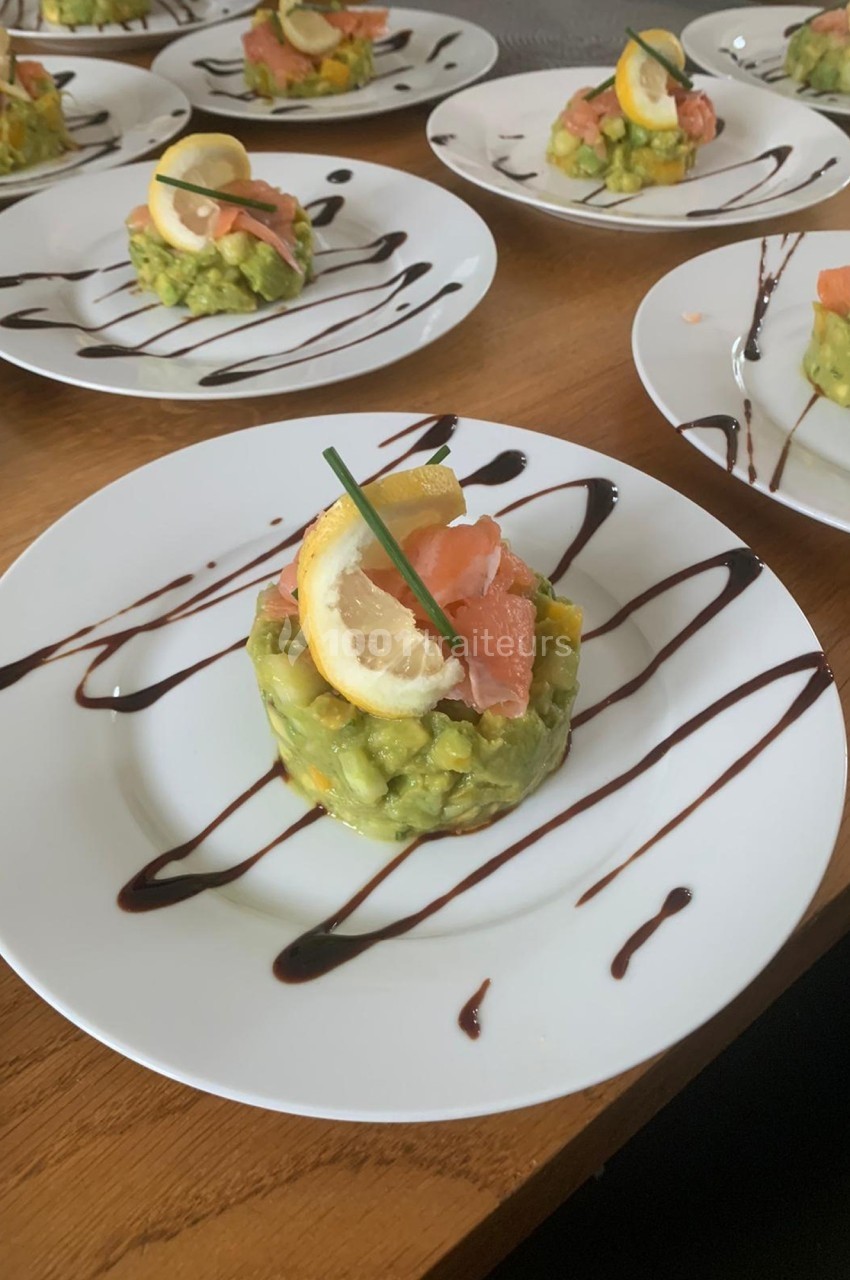 Assiette contenant un tartare d'avocat, saumon fumé, tranche de citron et filet de sauce balsamique.