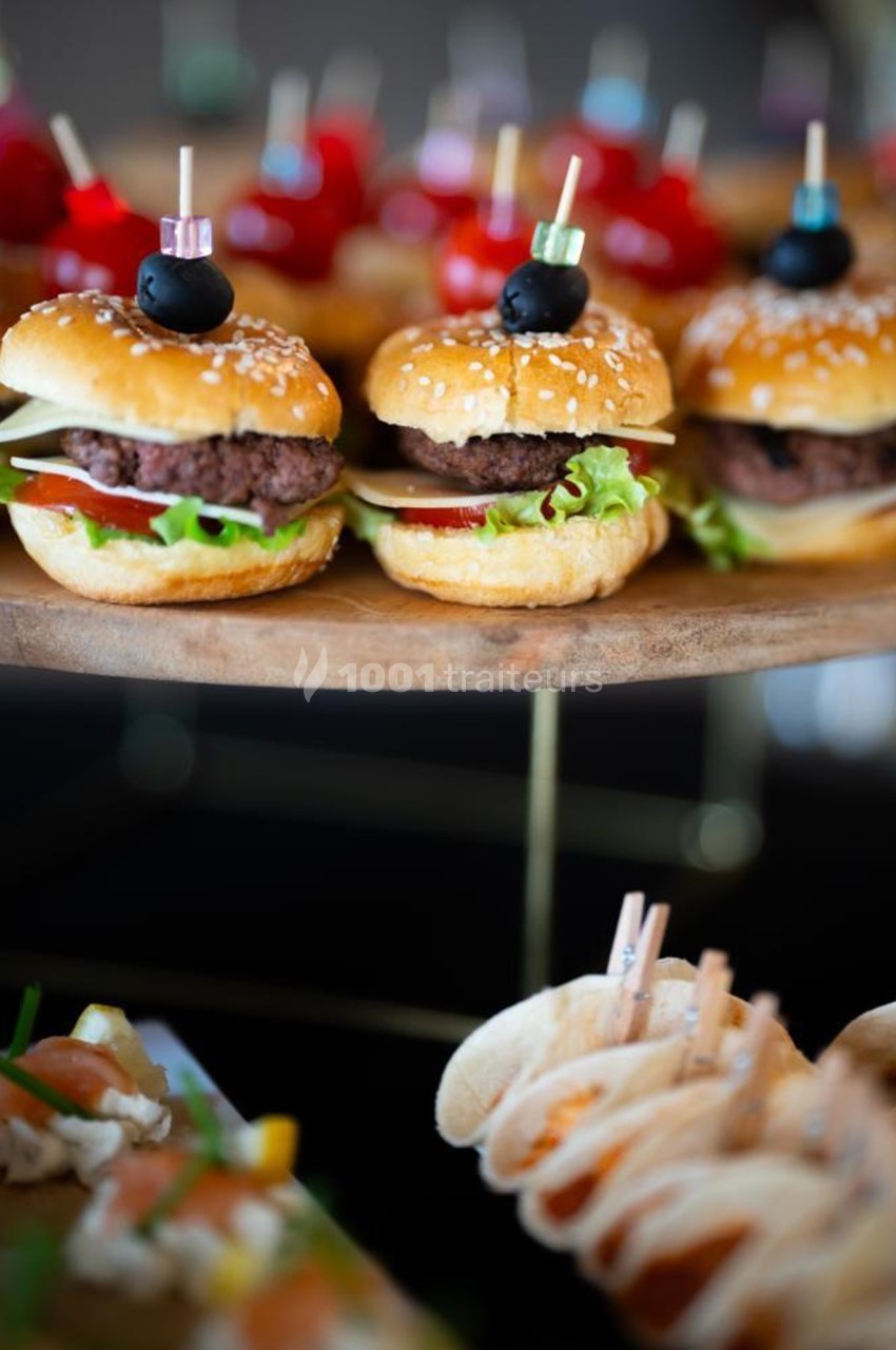 Mini burgers garnis de salade, tomate et steak, présentés sur un plateau en bois avec d'autres amuse-bouches.