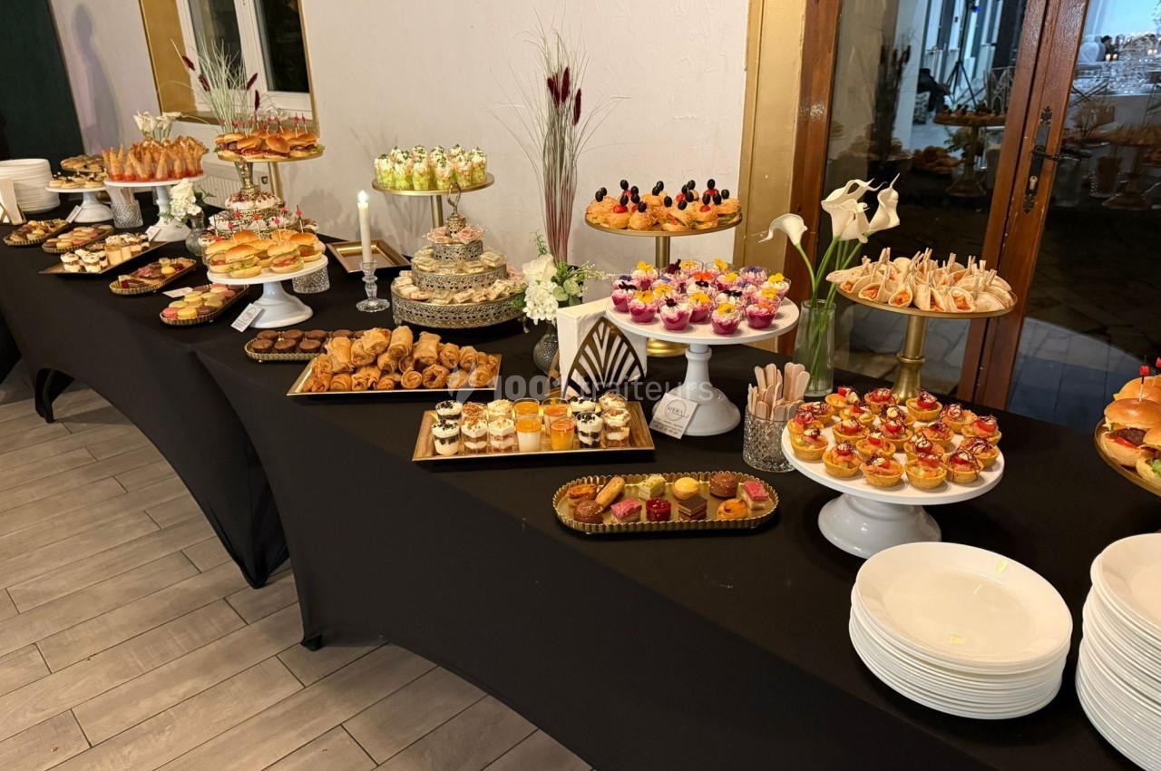 Buffet de desserts et amuse-bouches variés disposés sur des tables noires avec présentoirs et décorations florales.