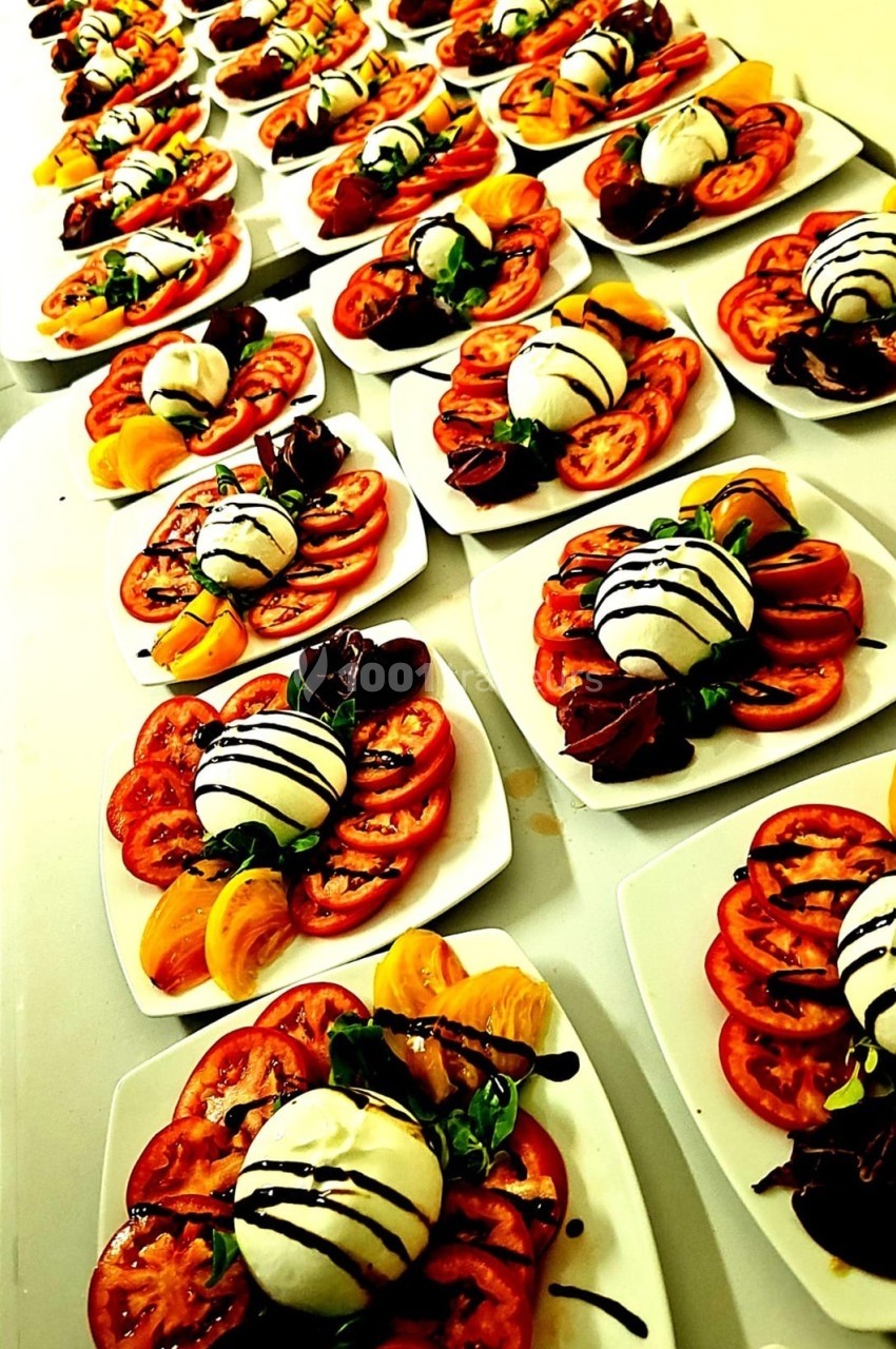 Assiettes alignées de salades caprese avec tomates, mozzarella, basilic et filet de vinaigre balsamique.