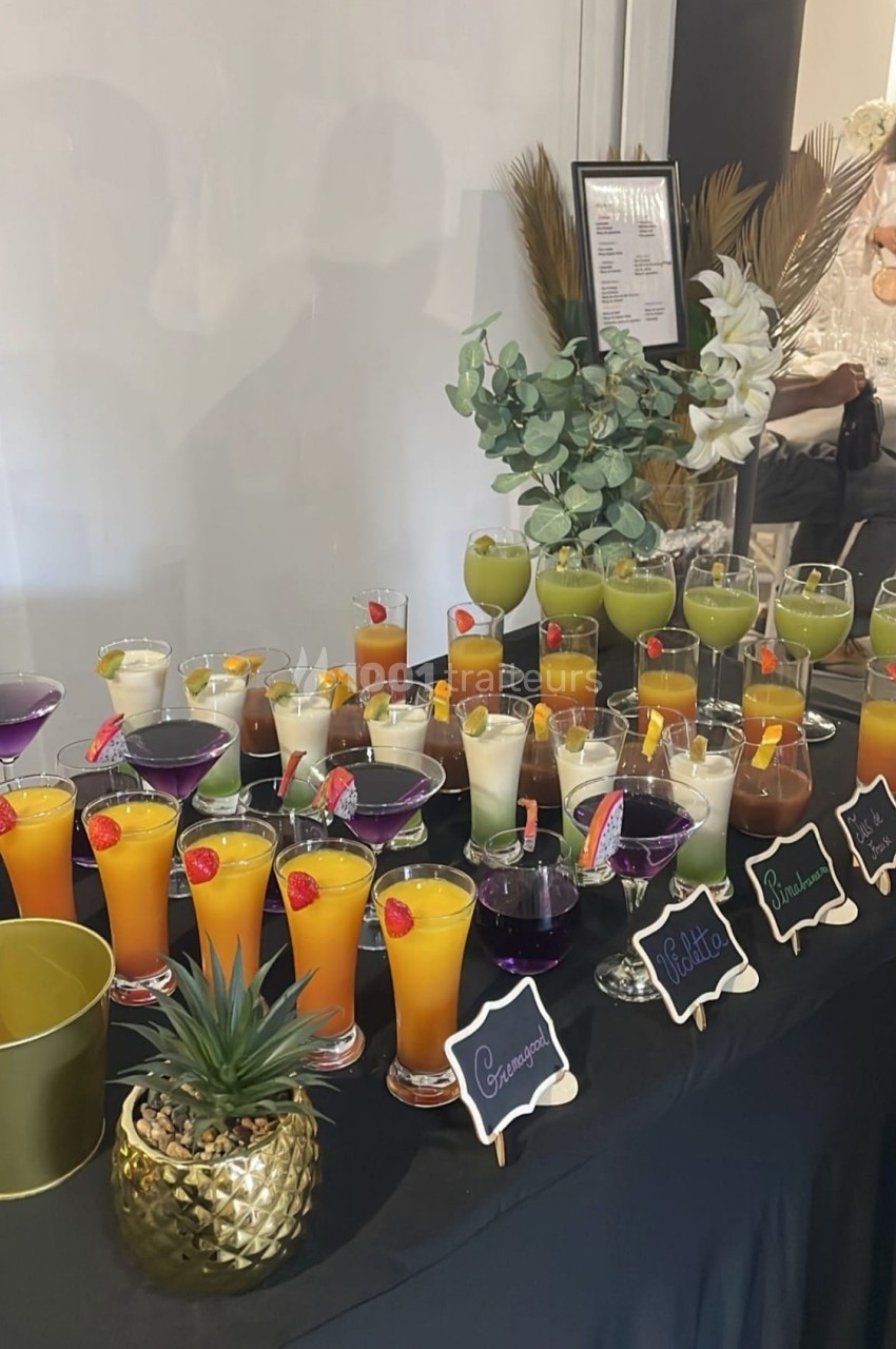 Buffet de cocktails colorés disposés sur une table noire, décorée de plantes et d'éléments dorés.