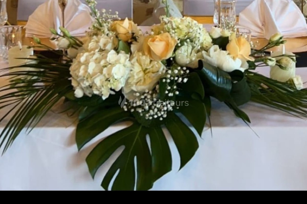 Arrangement floral avec roses jaunes, hortensias blancs, feuillage tropical et gypsophile sur une table dressée.