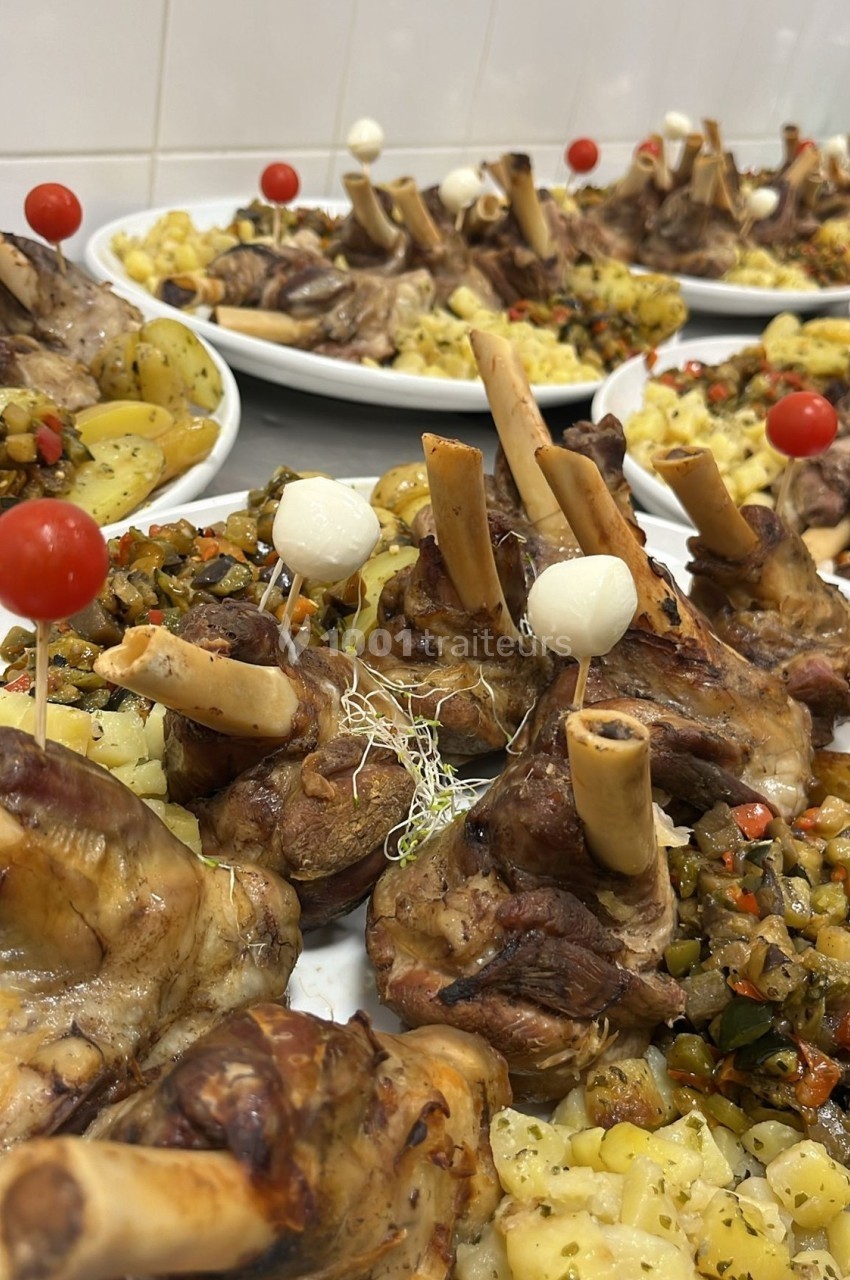 Assiettes de jarrets d'agneau rôtis accompagnés de pommes de terre et légumes, décorées de tomates cerises et oignons.