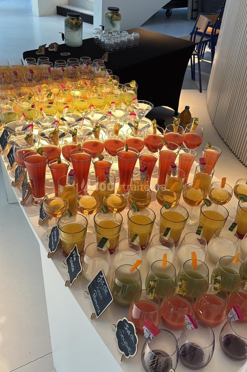 Buffet de cocktails colorés disposés sur une table blanche, avec des étiquettes indiquant les saveurs.