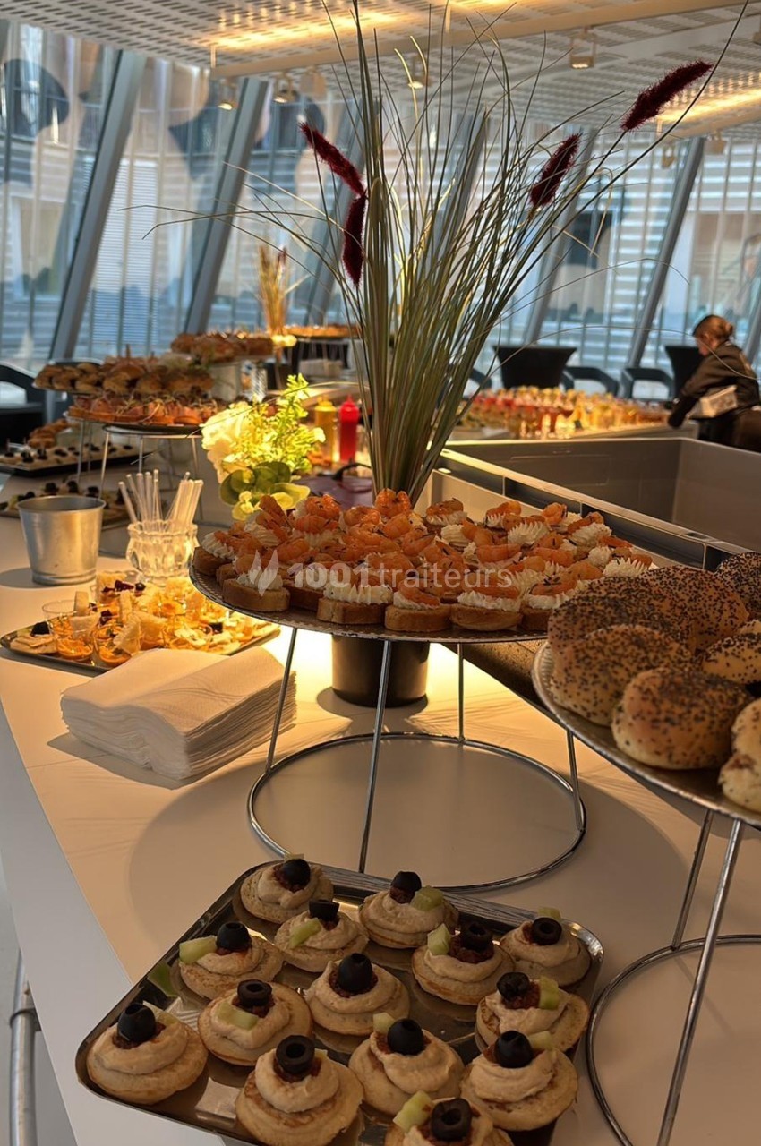 Buffet avec assortiments de viennoiseries, bagels, amuse-bouches et décorations végétales dans un espace lumineux.