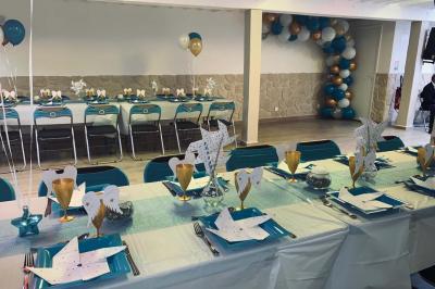 Salle spacieuse avec sol en parquet, murs en pierre et poutres blanches apparentes, éclairée par des lumières modernes.