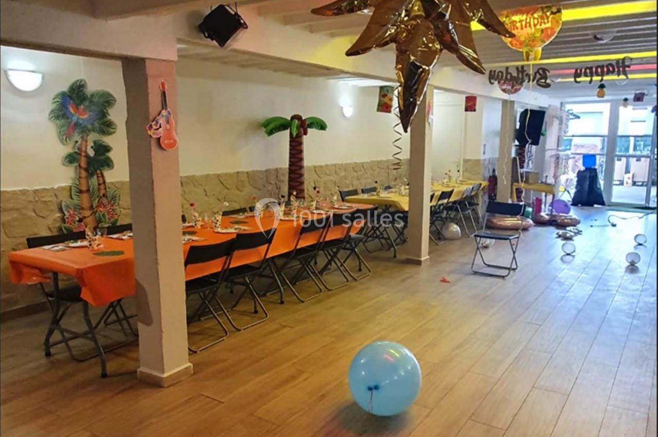 Salle décorée pour une fête avec tables dressées, ballons colorés et ornements tropicaux.