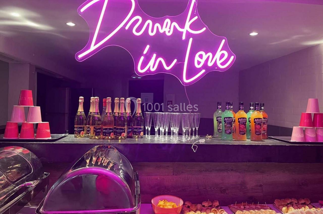 Buffet avec boissons, verres, amuse-bouches et enseigne néon rose affichant ’Drunk in Love’.