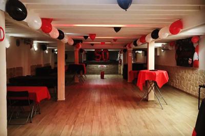 Salle spacieuse avec sol en parquet, murs en pierre et poutres blanches apparentes, éclairée par des lumières modernes.