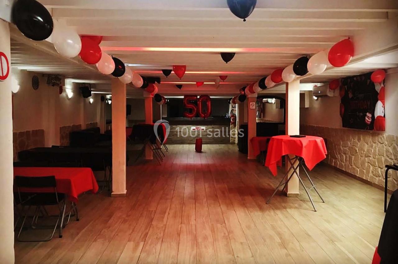 Salle décorée pour un événement avec des ballons rouges, noirs et blancs, et le chiffre 50 en décoration centrale.