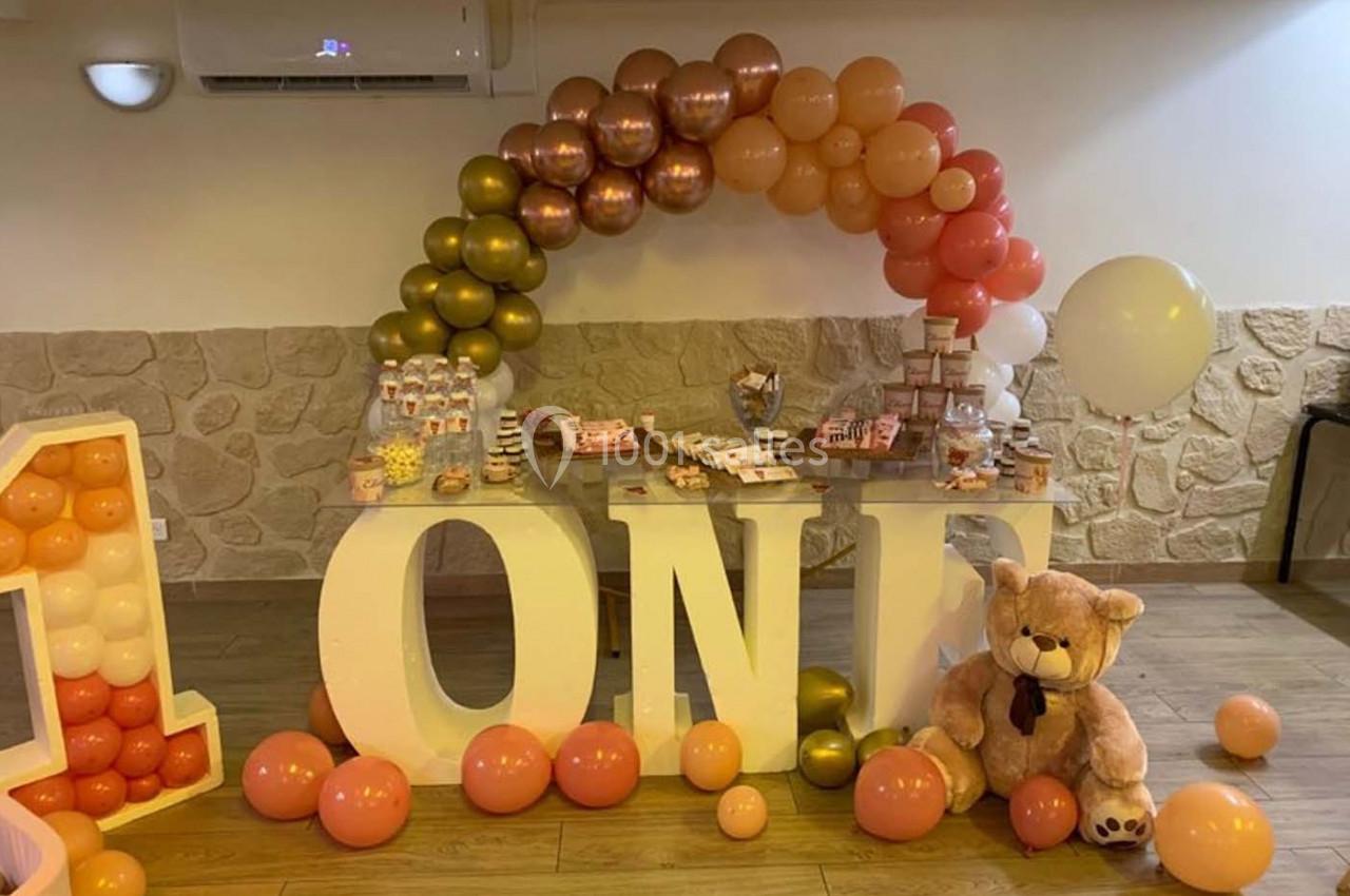 Décoration de fête avec ballons colorés, grande inscription ’ONE’, table de friandises et peluche d'ours.