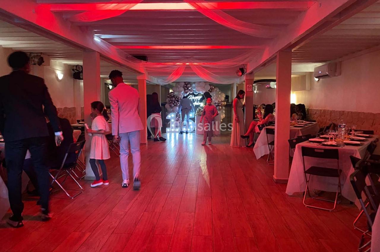 Salle de réception décorée avec des tables dressées, des invités debout et un éclairage rouge tamisé.