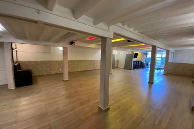 Salle spacieuse avec sol en parquet, murs en pierre et poutres blanches apparentes, éclairée par des lumières modernes.