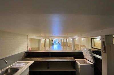 Salle spacieuse avec sol en parquet, murs en pierre et poutres blanches apparentes, éclairée par des lumières modernes.