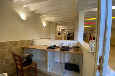 Salle spacieuse avec sol en parquet, murs en pierre et poutres blanches apparentes, éclairée par des lumières modernes.