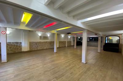 Salle spacieuse avec sol en parquet, murs en pierre et poutres blanches apparentes, éclairée par des lumières modernes.