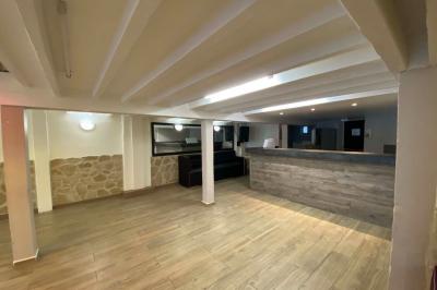 Salle spacieuse avec sol en parquet, murs en pierre et poutres blanches apparentes, éclairée par des lumières modernes.