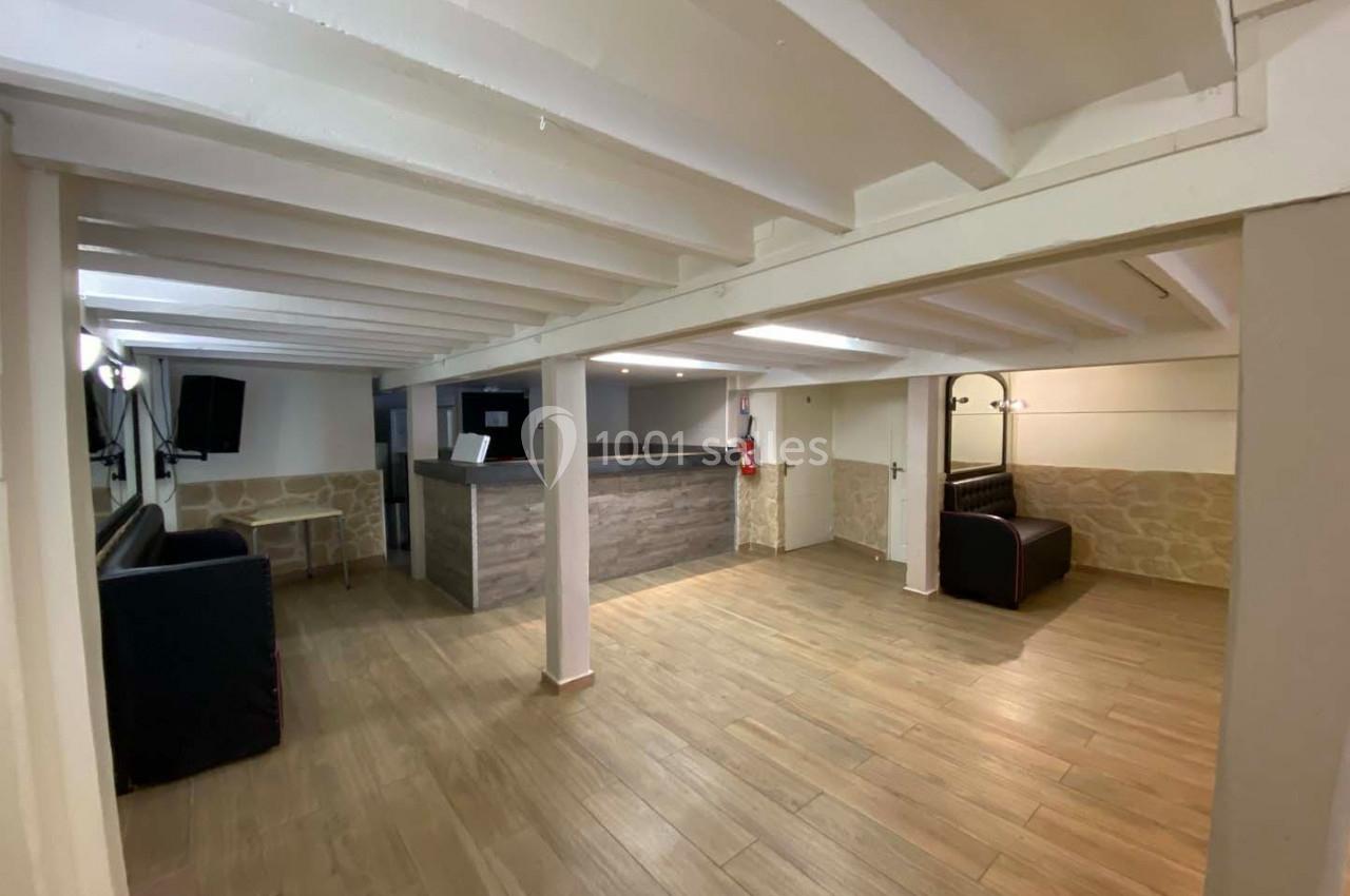 Salle lumineuse avec parquet, murs en pierre et poutres apparentes, aménagée avec un comptoir et des canapés.