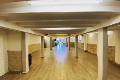 Salle spacieuse avec sol en parquet, murs en pierre et poutres blanches apparentes, éclairée par des lumières modernes.