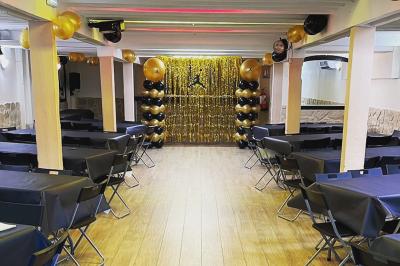 Salle spacieuse avec sol en parquet, murs en pierre et poutres blanches apparentes, éclairée par des lumières modernes.